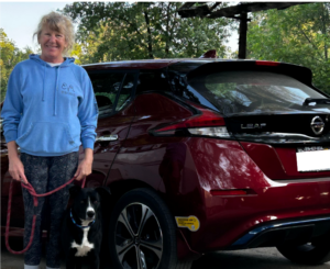 Woman and dog posing next to an electric car